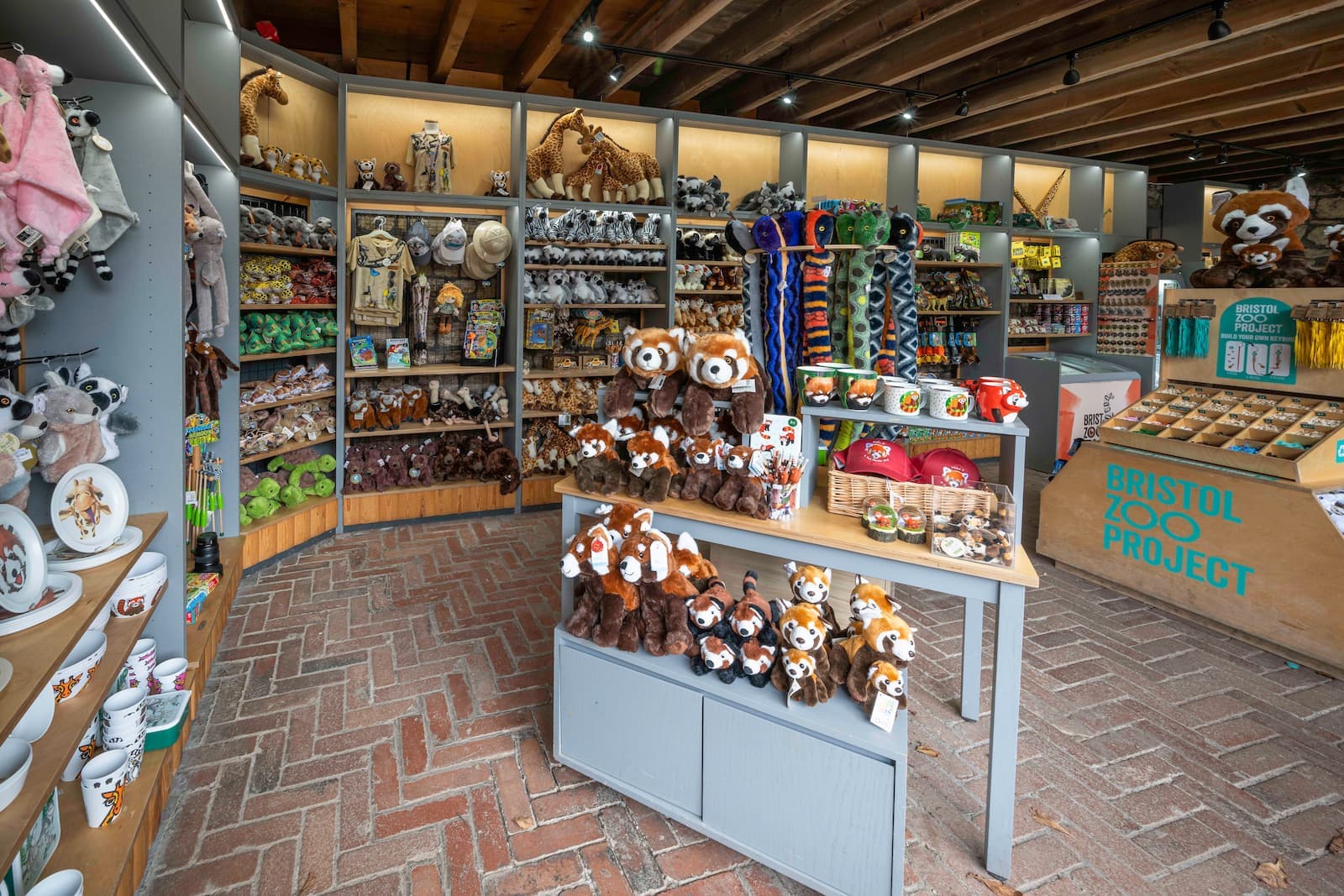 A zoo gift shop with plush toys, mugs, and souvenirs on display. Shelves are filled with animal-themed items under wooden beams.
